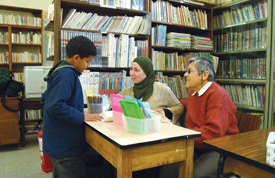 Sister Simone Verges, M.S.O.L.A. and Lynda, the assistant librarian, help Ahmed, 10, check out a book.